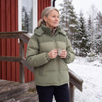 Kvinna i Cord Puffer Jacket i salviagrön med kaffe på stugtrappan i snön