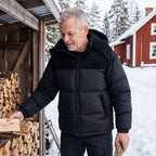 Man i Cord Puffer Jacket i svart staplar ved vid stugan i snön
