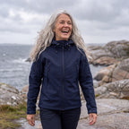 Kvinde i marineblå Utility Softshell Jacket på en blæsende gåtur langs kysten