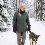 Frau mit schwarzen Skihandschuhen beim Gassigehen in einem verschneiten Wald